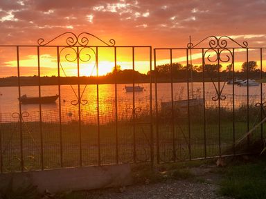 A sunset over a body of water with boats and a decorative iron gate in the foreground at Harbour View Mudeford Christchurch