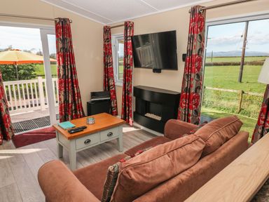 A living room with a sofa coffee table wall-mounted TV and windows overlooking a garden at Mountain View Lodge Tavernspite near Narberth