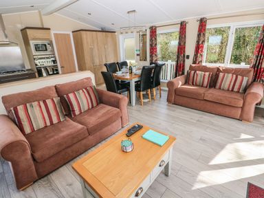 A living room with two brown sofas a wooden coffee table and a dining table with six black chairs at Mountain View Lodge Tavernspite near Narberth