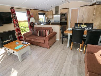 A living area with brown sofas a wooden coffee table a dining table with black chairs and a kitchen at Mountain View Lodge Tavernspite near Narberth