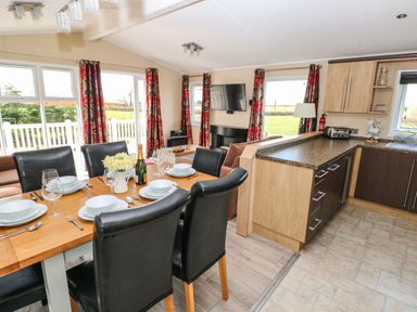 A dining area with a wooden table set with dinnerware and black chairs next to a kitchen with wood cabinets and countertops at Mountain View Lodge Tavernspite near Narberth