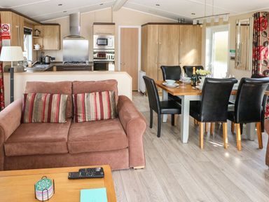 An open kitchen and dining area with a brown sofa, wooden dining table with black chairs, and kitchen appliances at Mountain View Lodge Tavernspite near Narberth