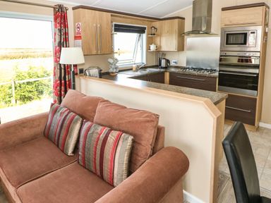 A kitchen area with wooden cabinets a gas stove built-in microwave and oven and a brown sofa with striped cushions at Mountain View Lodge Tavernspite near Narberth