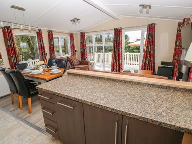 A dining area with a table set for four and a living room with a sofa and windows with red floral curtains at Mountain View Lodge in Tavernspite near Narberth