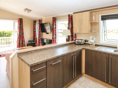 A kitchen with wood cabinets a toaster a hanging mug rack and a window overlooking a field at Mountain View Lodge Tavernspite near Narberth