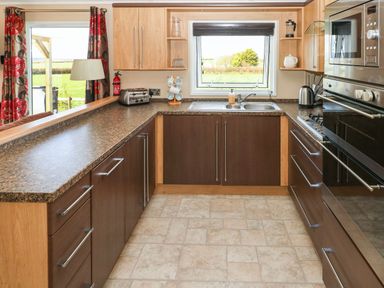 A kitchen with dark cabinets a toaster a kettle a microwave and oven a sink and a window overlooking a garden at Mountain View Lodge in Tavernspite near Narberth