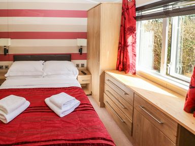 A bedroom with a double bed red bedspread wooden furniture and a window with red curtains at Mountain View Lodge Tavernspite near Narberth