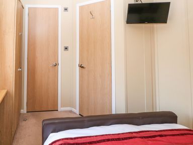 A bedroom with two wooden doors a wall-mounted television and a bed with a red blanket at Mountain View Lodge in Tavernspite near Narberth