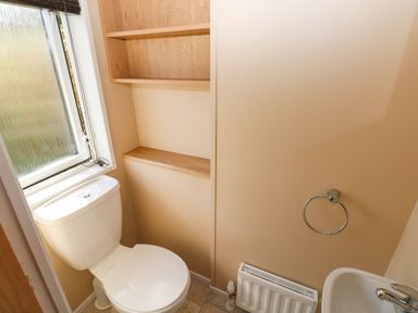 A small bathroom with a toilet near a window wooden shelves on the wall a sink with a towel ring and a radiator at Mountain View Lodge Tavernspite near Narberth
