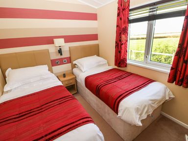 A bedroom with two single beds with red bed runners a wooden nightstand and a window with red curtains at Mountain View Lodge Tavernspite near Narberth