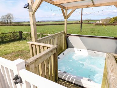 An outdoor hot tub under a wooden pergola with a view of fields and hills at Mountain View Lodge in Tavernspite near Narberth