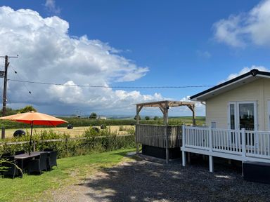 An outdoor area with a patio table and umbrella next to a building with a wooden deck and railings at Mountain View Lodge in Tavernspite near Narberth