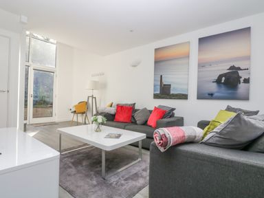 A living room with sofas red and green cushions white coffee table and large wall art at Sea Breeze 17 Gannel in Porthtowan