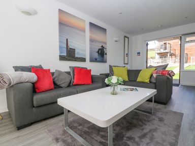 A living room with grey sofas red and green cushions and a white coffee table at Sea Breeze 17 Gannel in Porthtowan