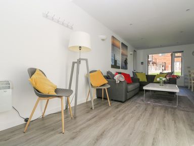 A living room with chairs, a floor lamp, a sofa with cushions, a coffee table, and large windows at Sea Breeze 17 Gannel in Porthtowan