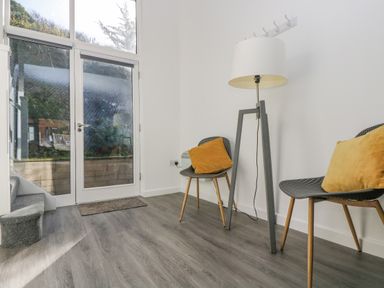 A corner with two chairs with cushions and a floor lamp next to a glass door at Sea Breeze 17 Gannel in Porthtowan
