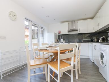 A kitchen with a dining table and six chairs plates and glasses on the table and appliances on the counters at Sea Breeze 17 Gannel in Porthtowan