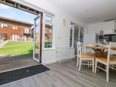 A dining area with a round wooden table and chairs next to open doors leading outside at Sea Breeze 17 Gannel in Porthtowan