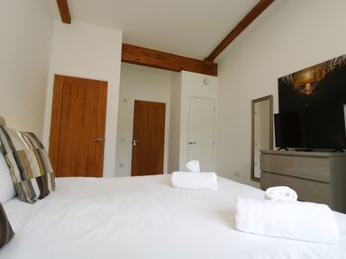 A bedroom with a bed with towels and cushions wooden doors a chest of drawers with a TV and a wall mirror at Sea Breeze 17 Gannel in Porthtowan