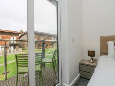 A bedroom with a bed, nightstand, lamp, and glass door leading to a balcony with two chairs at Sea Breeze 17 Gannel in Porthtowan