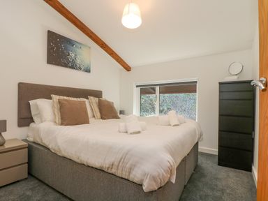 A bedroom with a large bed with pillows and rolled towels bedside tables a window and a black chest of drawers at Sea Breeze 17 Gannel in Porthtowan