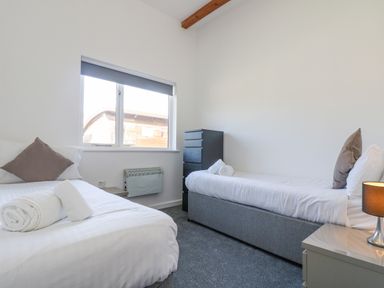 A bedroom with two single beds pillows rolled towels a bedside table with lamp and a chest of drawers at Sea Breeze 17 Gannel in Porthtowan