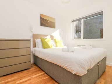 A bedroom with a bed with white linens and green pillows a chest of drawers and a window at Sea Breeze 17 Gannel in Porthtowan