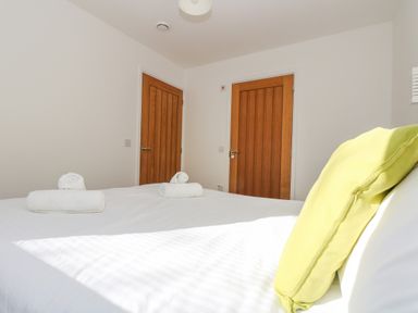 A bedroom with a bed covered in white sheets and yellow pillows with two wooden doors at Sea Breeze 17 Gannel in Porthtowan
