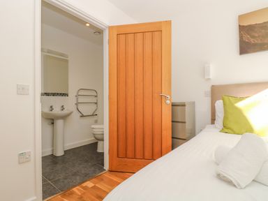 A bedroom with a bed and green pillow next to an open door showing a bathroom with a sink and toilet at Sea Breeze 17 Gannel in Porthtowan