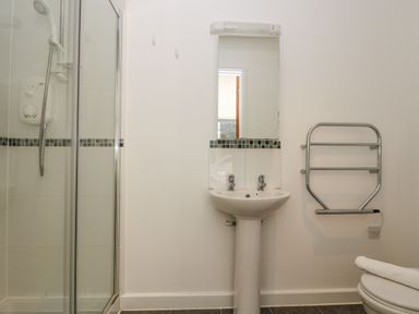 A bathroom with a shower, pedestal sink, mirror, towel rack and toilet at Sea Breeze 17 Gannel in Porthtowan