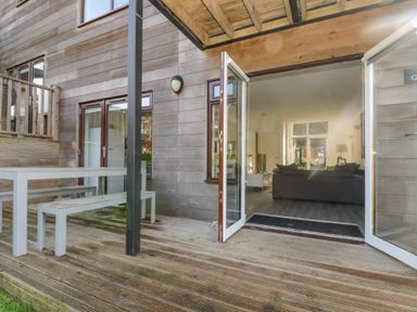 An outdoor wooden deck with a white table and benches leading into a living room with a sofa and a television at Sea Breeze 17 Gannel in Porthtowan
