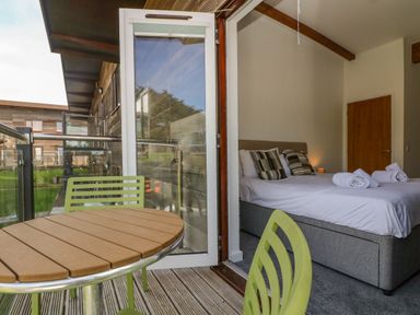 A bedroom with a made bed and rolled towels visible through an open door leading to a balcony with a table and chairs at Sea Breeze 17 Gannel in Porthtowan