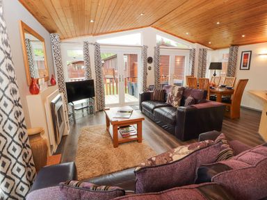 A living room with sofas coffee table and dining table near windows and doors at Fell View Lodge in Troutbeck