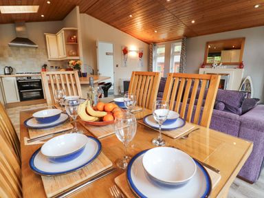 A dining table set with plates bowls glasses and fruit in an open kitchen and living room at Fell View Lodge in Troutbeck