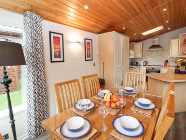 A dining area with a wooden table set for six and a kitchen with wooden cabinets in the background at Fell View Lodge in Troutbeck