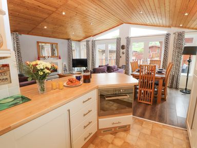 A kitchen counter with croissants orange juice and a French press next to a dining table and living room at Fell View Lodge in Troutbeck
