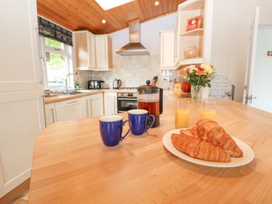 A kitchen with a wooden countertop holding two blue mugs a French press two glasses of orange juice and a plate of croissants at Fell View Lodge in Troutbeck