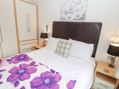A bedroom with a double bed a floral blanket two bedside tables with lamps and a wardrobe at Fell View Lodge in Troutbeck