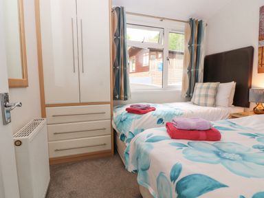 A bedroom with two single beds a wardrobe and a window showing a wooden building outside at Fell View Lodge in Troutbeck