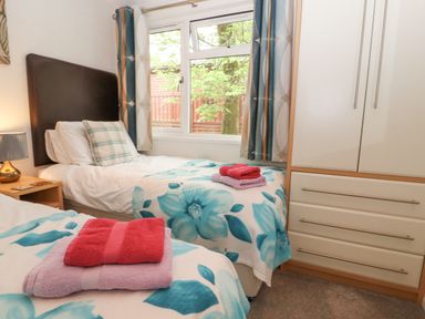 A bedroom with two single beds with floral blankets and folded towels a bedside table with a lamp and a white wardrobe at Fell View Lodge in Troutbeck