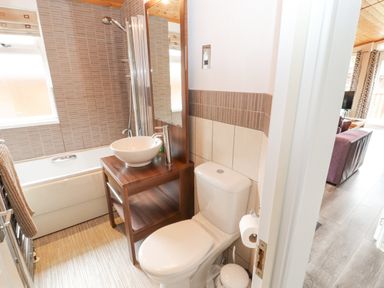 A bathroom with a toilet a wooden sink vanity a bathtub with shower and a towel rack at Fell View Lodge in Troutbeck