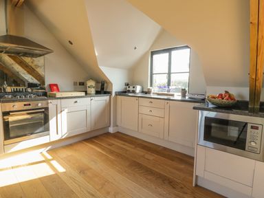 A kitchen with white cabinets wooden floor and a window above the counter at The Coach House in St Columb Major