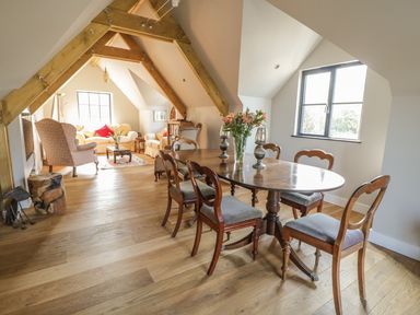 A dining area with wooden table and chairs and a seating area with sofas and armchairs in a room with exposed beams at The Coach House in St Columb Major