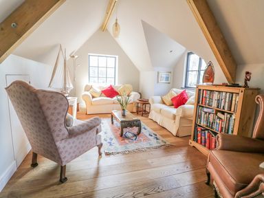 A living room with sofas armchairs a coffee table bookshelf and decorative boat at The Coach House in St Columb Major