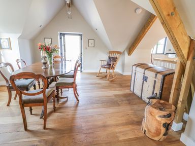 A dining area with a wooden table and chairs a rocking chair a wooden chest and exposed beams at The Coach House in St Columb Major