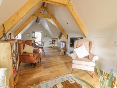 A living area with wooden beams a brown armchair a pink patterned armchair a bookshelf and a dining table at The Coach House in St Columb Major
