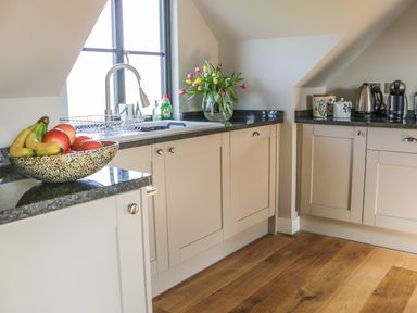 A kitchen with a fruit bowl bananas and apples a sink flowers on the counter and kitchen appliances at The Coach House in St Columb Major