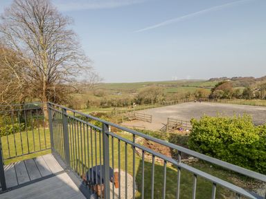 A balcony overlooking a fenced field with trees and green hills in the background at The Coach House in St Columb Major