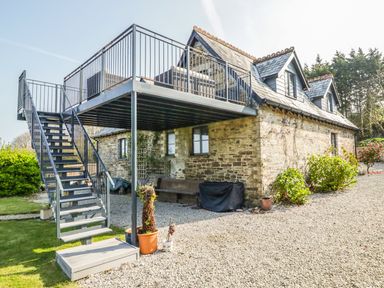 An outdoor metal staircase leading to a raised balcony attached to a stone house with gravel and plants around at The Coach House in St Columb Major
