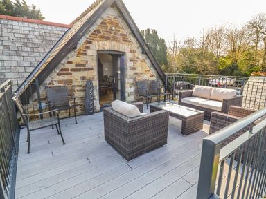 An outdoor seating area on a rooftop deck with wicker furniture and metal chairs at The Coach House in St Columb Major